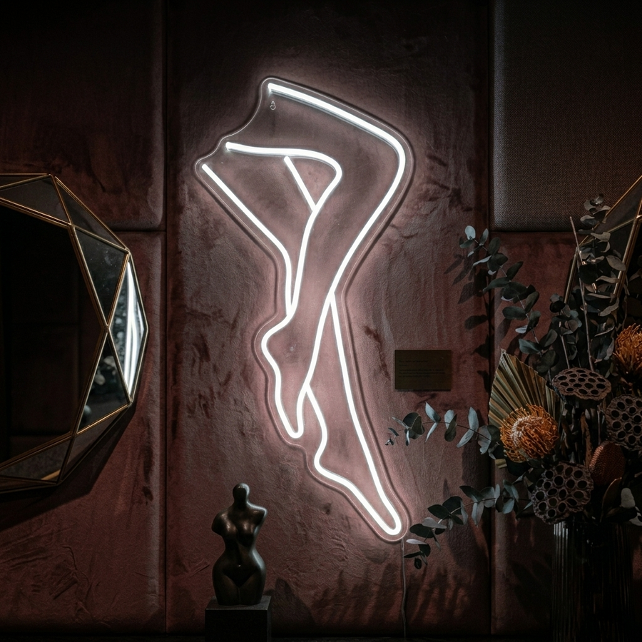 A real product photograph of the glowing red "Sexy Legs Lady" neon sign mounted on a textured wall above a wooden table with a floral arrangement and mirror.