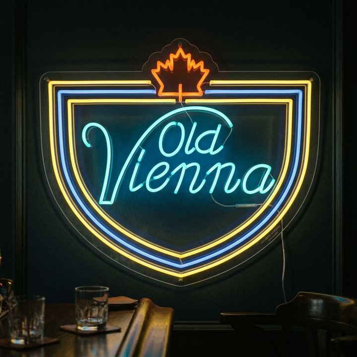 A close-up photograph of a mounted Old Vienna Beer neon sign with a glowing beaver logo and blue, red, and yellow text, displayed on a wooden plank wall in a dimly lit bar setting.