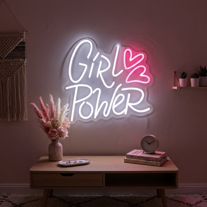 The 'Girl Power Hearts' neon sign glowing brightly with pink and white light against a slightly distressed dark wall, showcasing its physical appearance and mounting details.