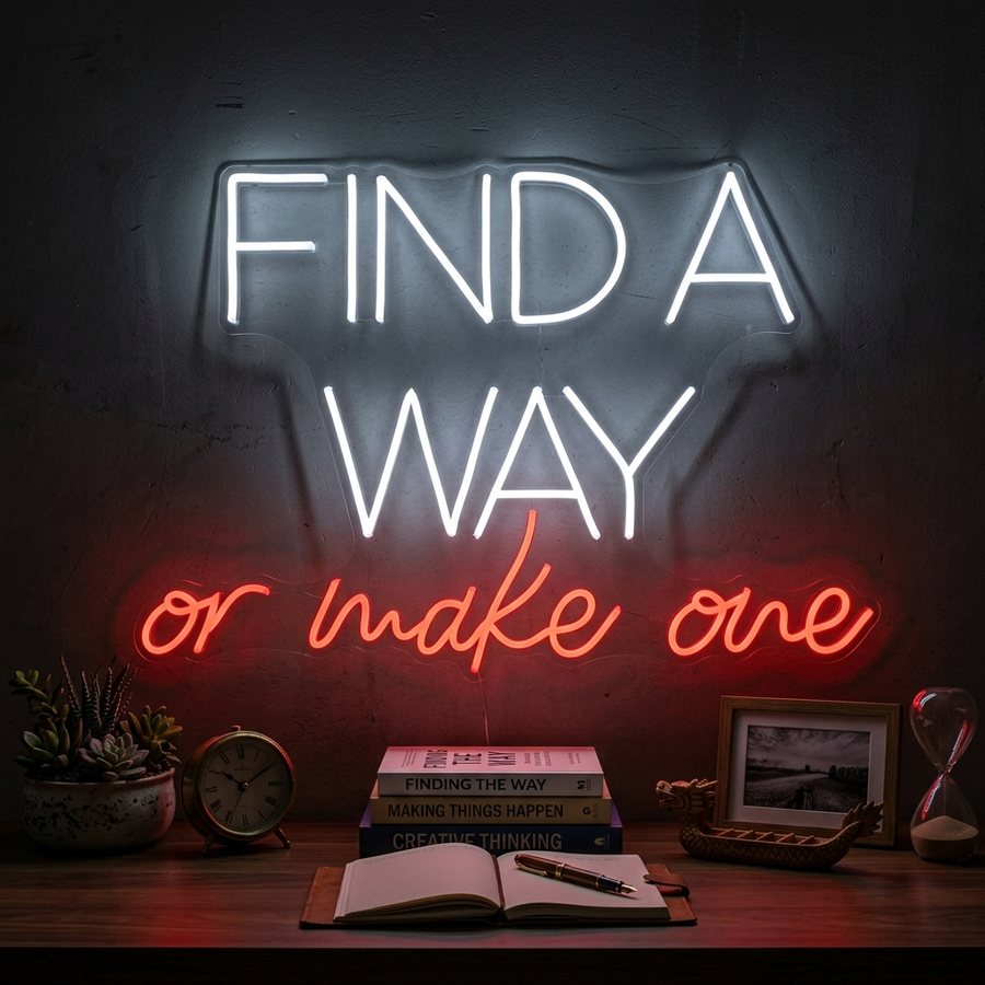 A bright pink 'Find A Way Or Make One' neon sign glows on a textured gray wall above a stack of motivational books in a modern home office setting.