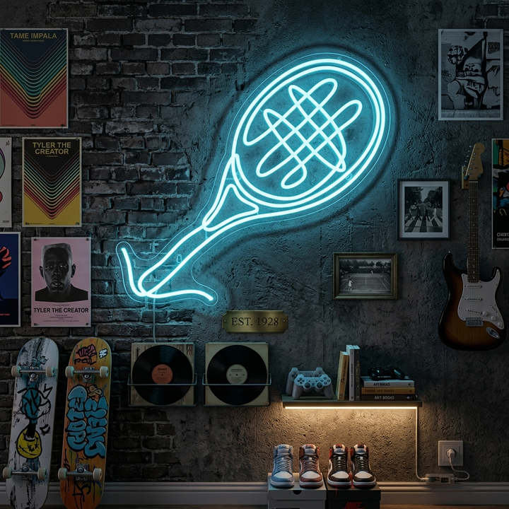 A glowing blue neon sign depicting a tennis racket and ball mounted on a wall above a wooden desk with books.