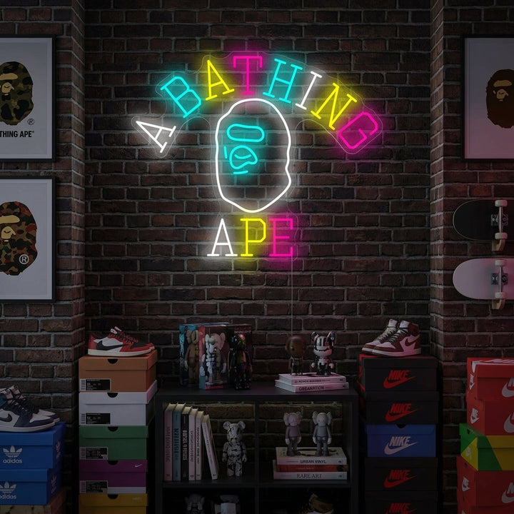 A glowing blue 'Bathing Ape' neon sign displaying the classic Ape Head logo, mounted on a rustic brick wall in a cool lifestyle room setting above a modern sofa.