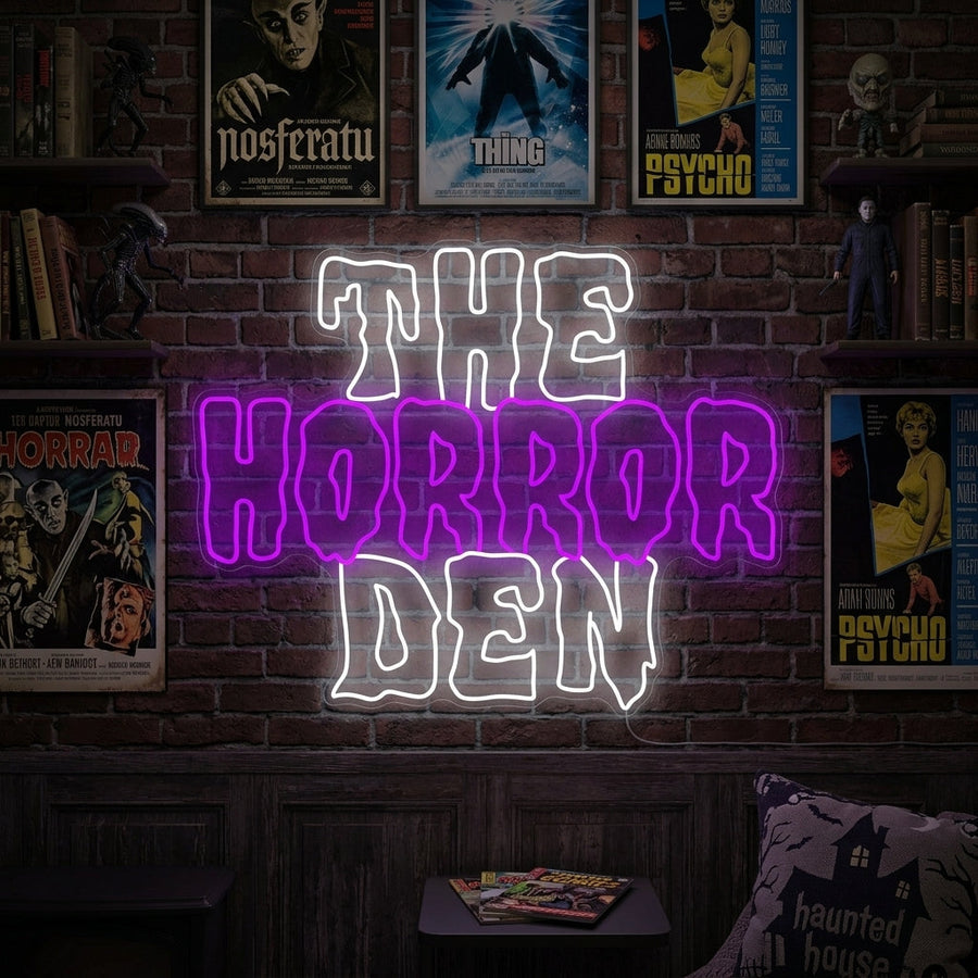 "The Horror Den" neon sign glowing on a wall in a moody, dark room with a plush armchair and spooky decorations.