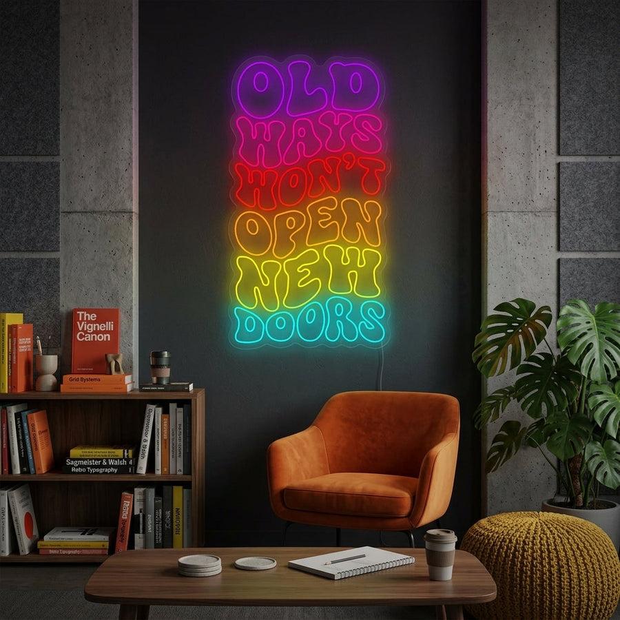 A stylish motivational neon sign that reads "Old Ways Won't Open New Doors" is mounted on a textured brick wall in a cozy home office setup, casting an inspiring glow. (Generated mockup)