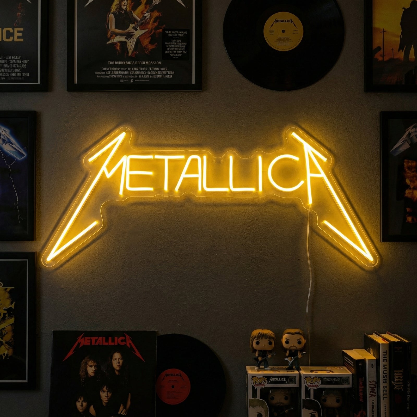 Real handcrafted glowing Metallica neon sign showing physical tubing and acrylic backboard mounted on a wall in a lived-in room.