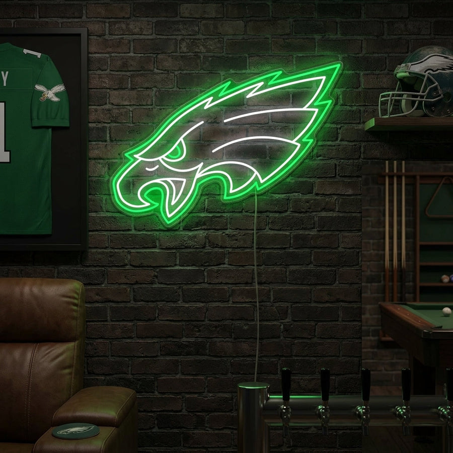 A candid, well-lit photo of an "Eagles" neon sign mounted on a brick wall in a cozy home game room setting, next to sports memorabilia.