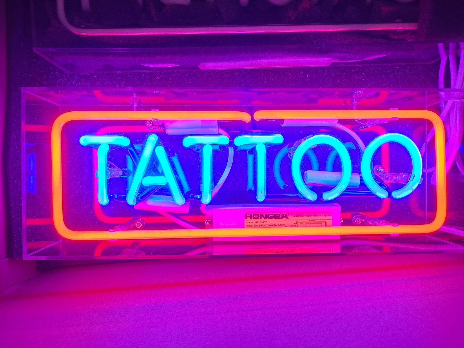 Close-up view of the glowing blue and red "Tattoo" neon sign in its clear box, highlighting the intricate glass tubes and components.