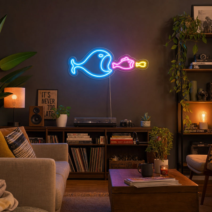 A glowing blue 'Big Fish Eat Small Fish' neon sign depicting a large fish about to eat a smaller one, mounted on a dark wall above a modern credenza with books and a plant.