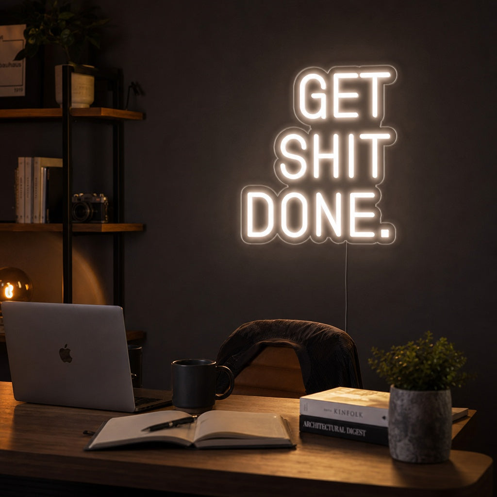 A 'Get Shit Done' neon sign glowing brightly on a brick wall above a productivity-focused desk setup.