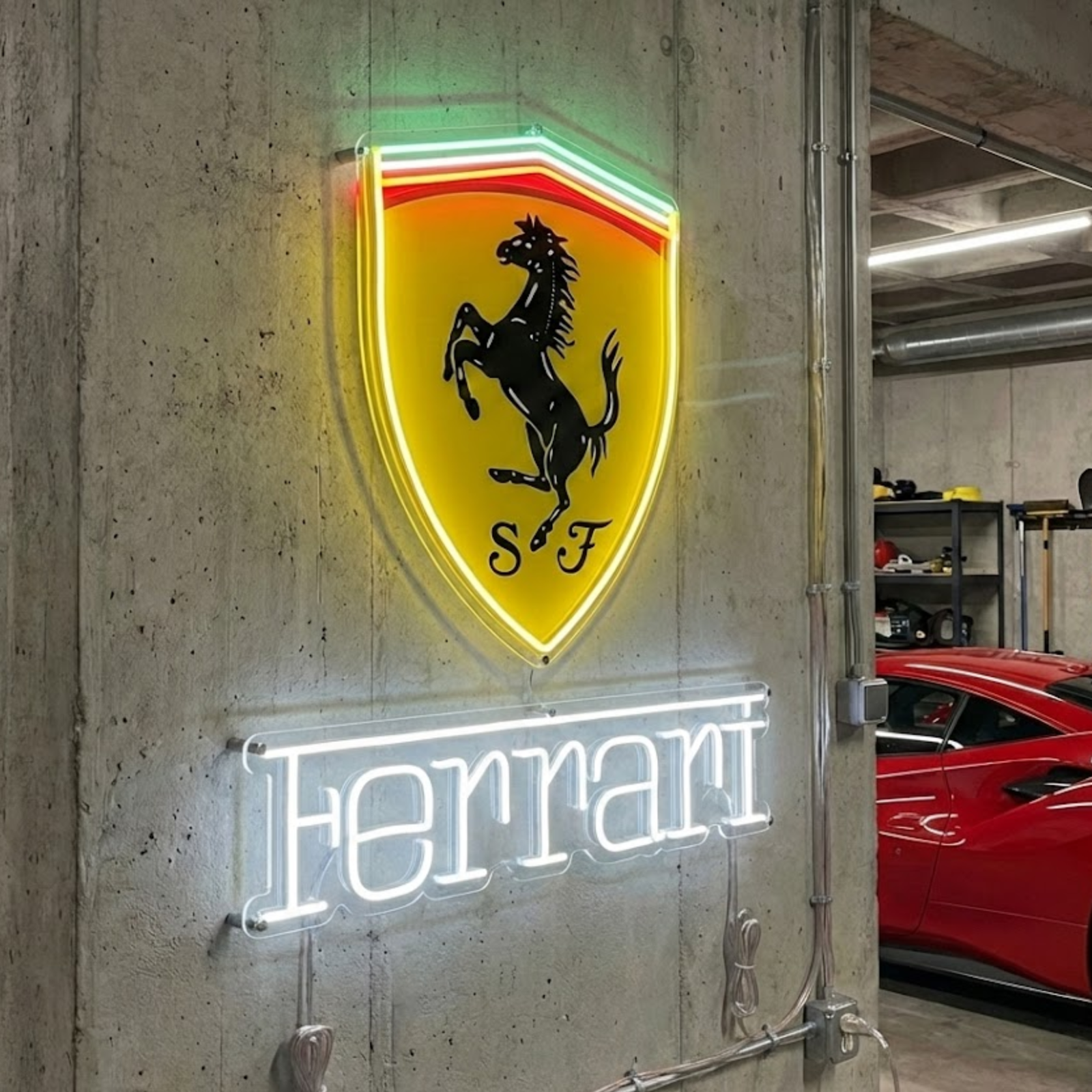 A natural photograph of the illuminated Sports Car Crest neon sign in a concrete-walled garage, with the side of a luxury sports car visible nearby.