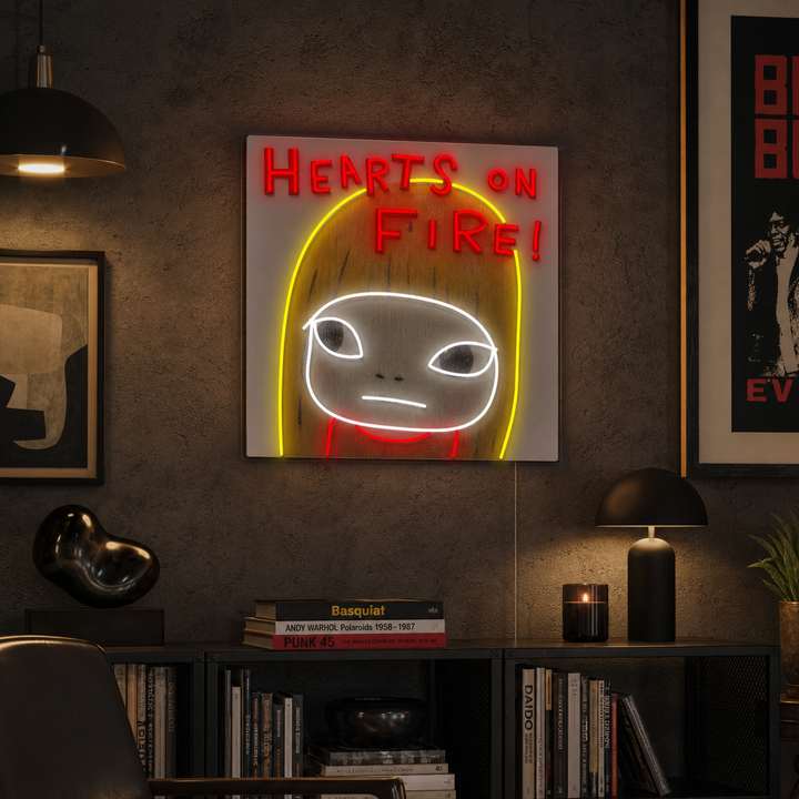 Hearts On Fire illuminated sign with detailed fiery graphics on clear backing, mounted on a living room wall above modern furniture.
