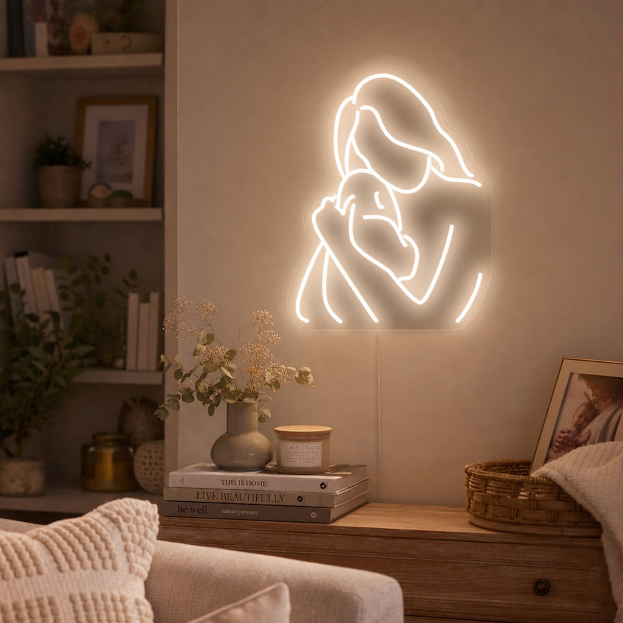 Lifestyle image of a warm glowing 'Mum Hug Mother Baby' neon sign mounted on a nursery wall above a crib.