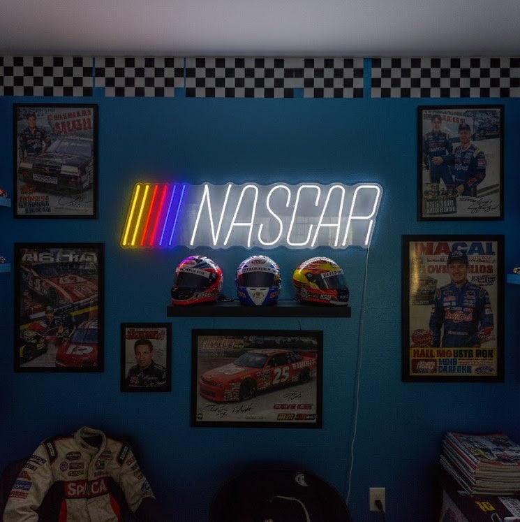 Official NASCAR neon sign glowing red, yellow, and blue, mounted on a rustic wood wall in a custom garage
