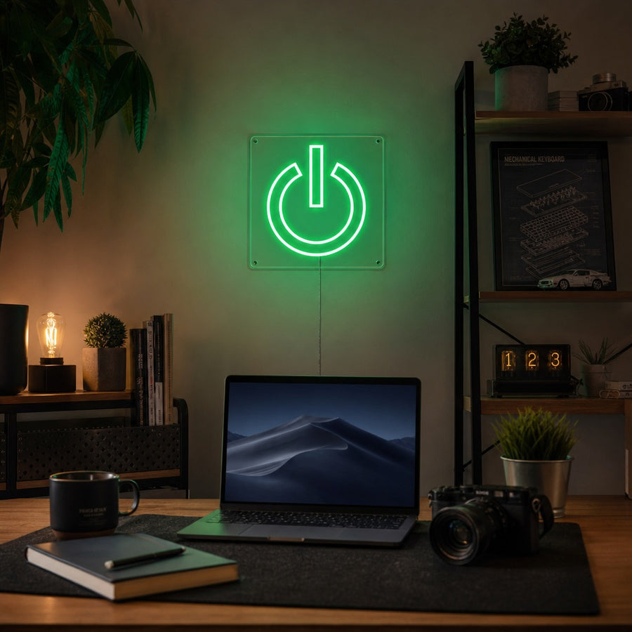 A vibrant green neon sign depicting a power symbol glowing on a dark wall above a gaming desk with a monitor.