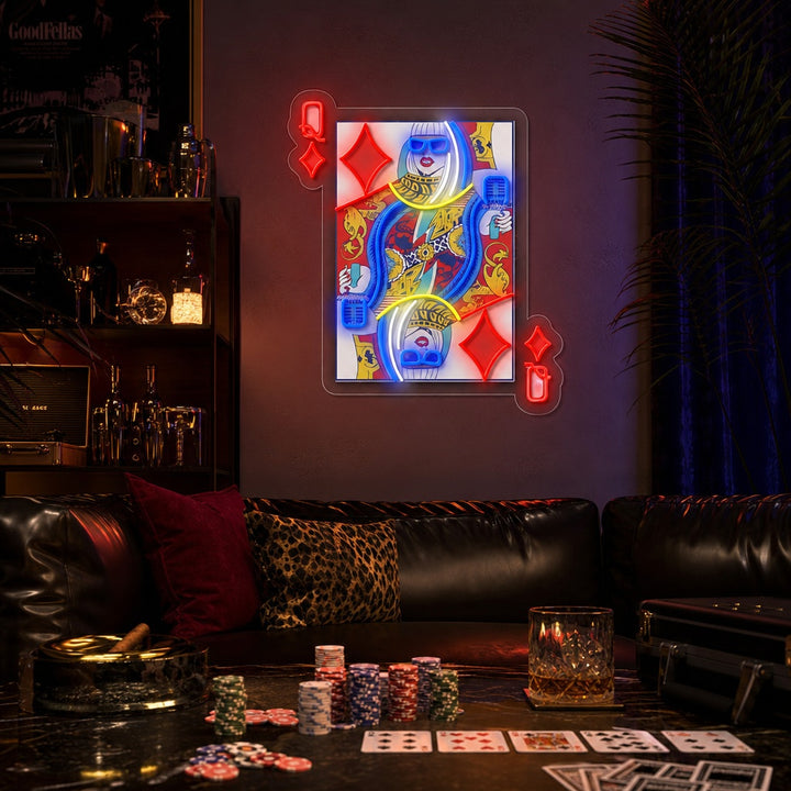 Close-up photograph of a 'Q Of Glam' UV print neon sign featuring a queen of clubs playing card design with pop star details on a decorative stand next to a potted plant.