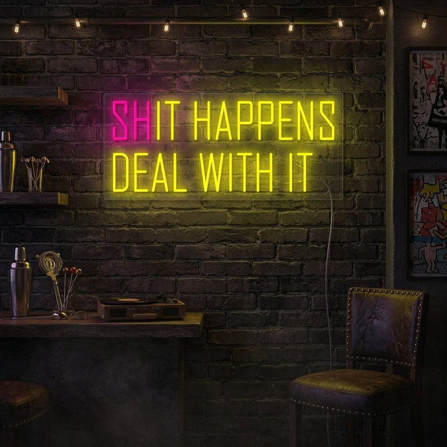A candid 'Shit happens It happens' neon sign glows on a wall in a relaxed, bohemian-style living room, creating a humorous focal point above a comfortable armchair and next to some leafy plants.