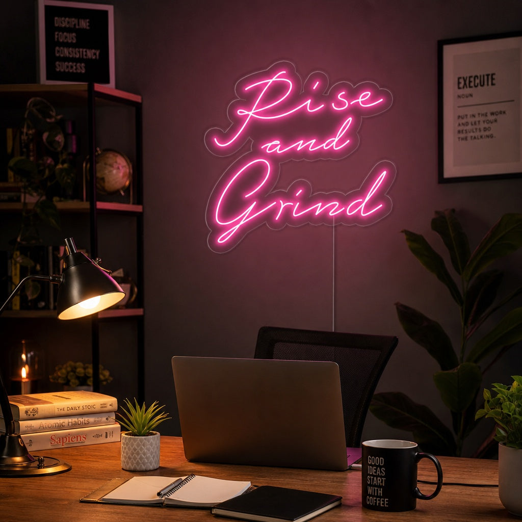 “Rise And Grind” motivational neon sign in bright yellow script glowing on a dark blue bedroom wall above a desk and bedside lamp