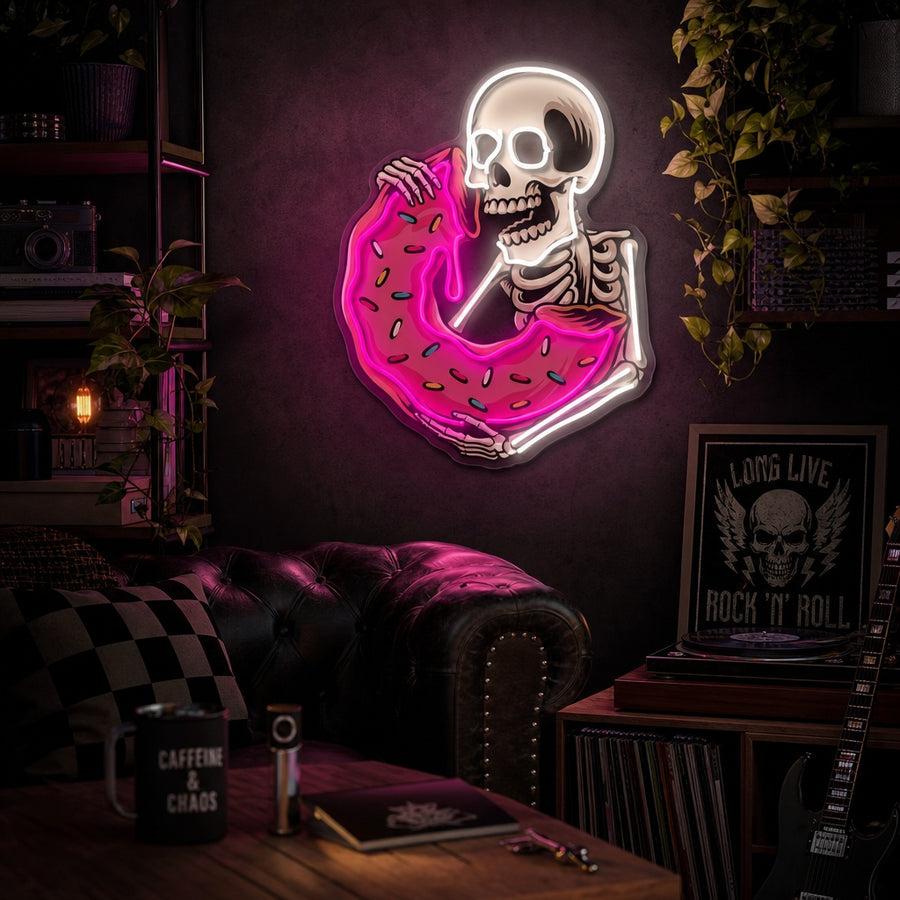 A vibrant UV print neon sign depicting a skull eating a colorful donut, glowing on an exposed brick wall above a cozy table setting with mugs and plants.