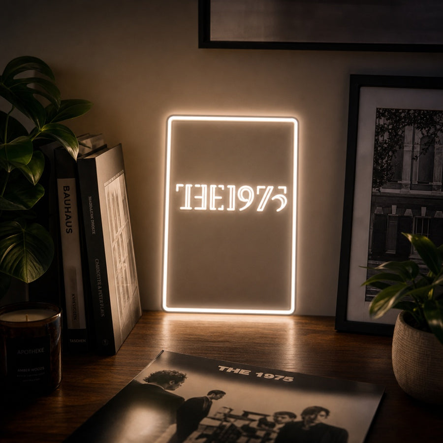 A glowing 'The 1975' neon sign in white text, centered on a light wooden background.