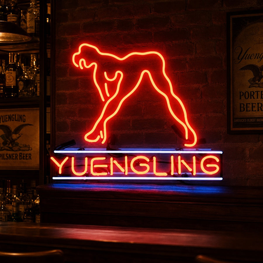 A close-up photograph of a fabricated 'Yuengling Live Nudes Girl' neon sign, featuring detailed tube shaping, visible wiring, and a central transformer, unlit.