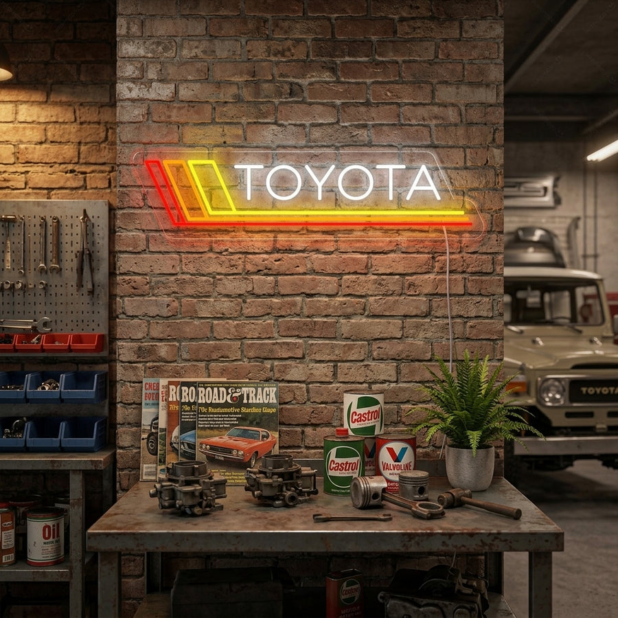 A glowing 'TOYOTA' neon sign with red tubing mounted on a wood-paneled wall above a desk with various automotive collectibles in a modern room, with visible wall glow.
