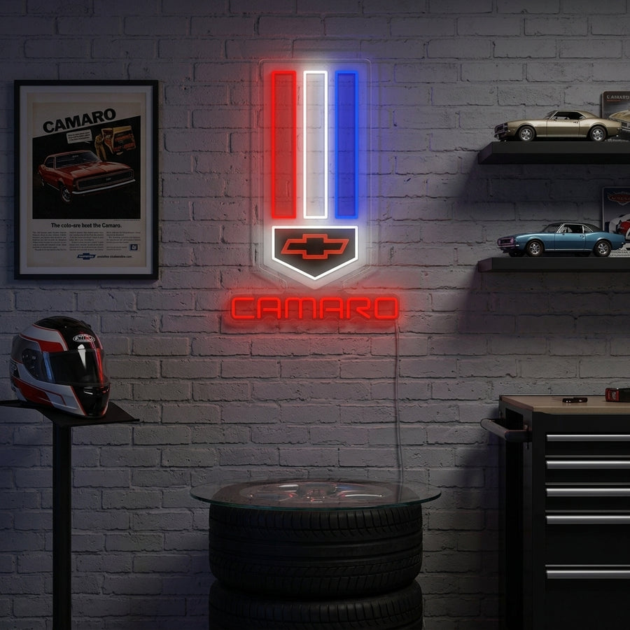 A glowing red and yellow Chev-Car neon sign featuring the classic bow-tie style design mounted on a wall in a decorated garage setting.