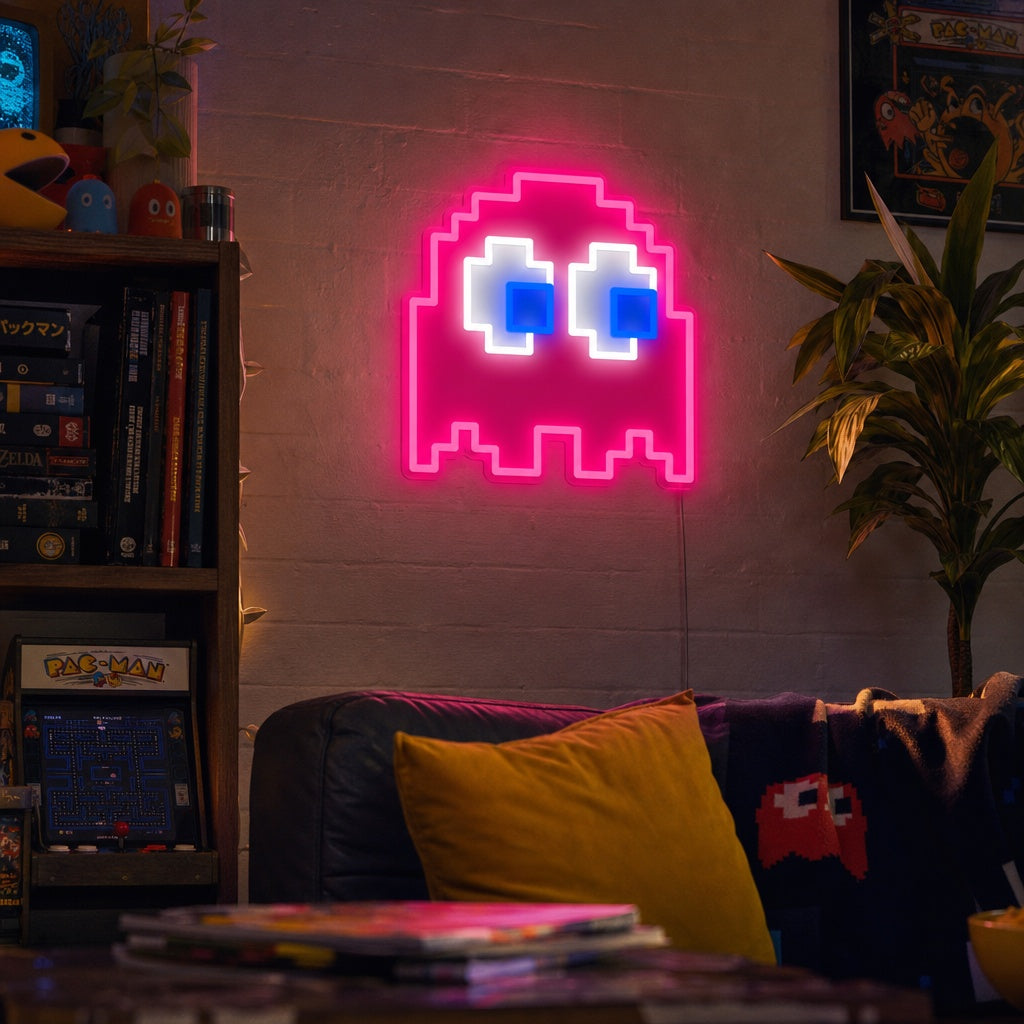 A vibrant arcade ghost neon sign glowing blue on a dark brick wall in a well-decorated gaming room setup.