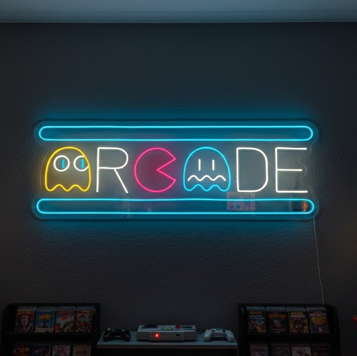 A real, glowing blue and pink Arcade Ghost neon sign on a clear acrylic backing, hanging on a wall in a dimly lit game room.