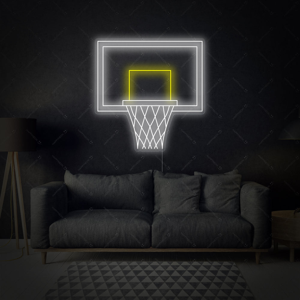 A glowing red neon sign showing a simplified graphic of a basketball hoop and net with an orange basketball above it, displayed against a dark blurred background and a wooden surface.
