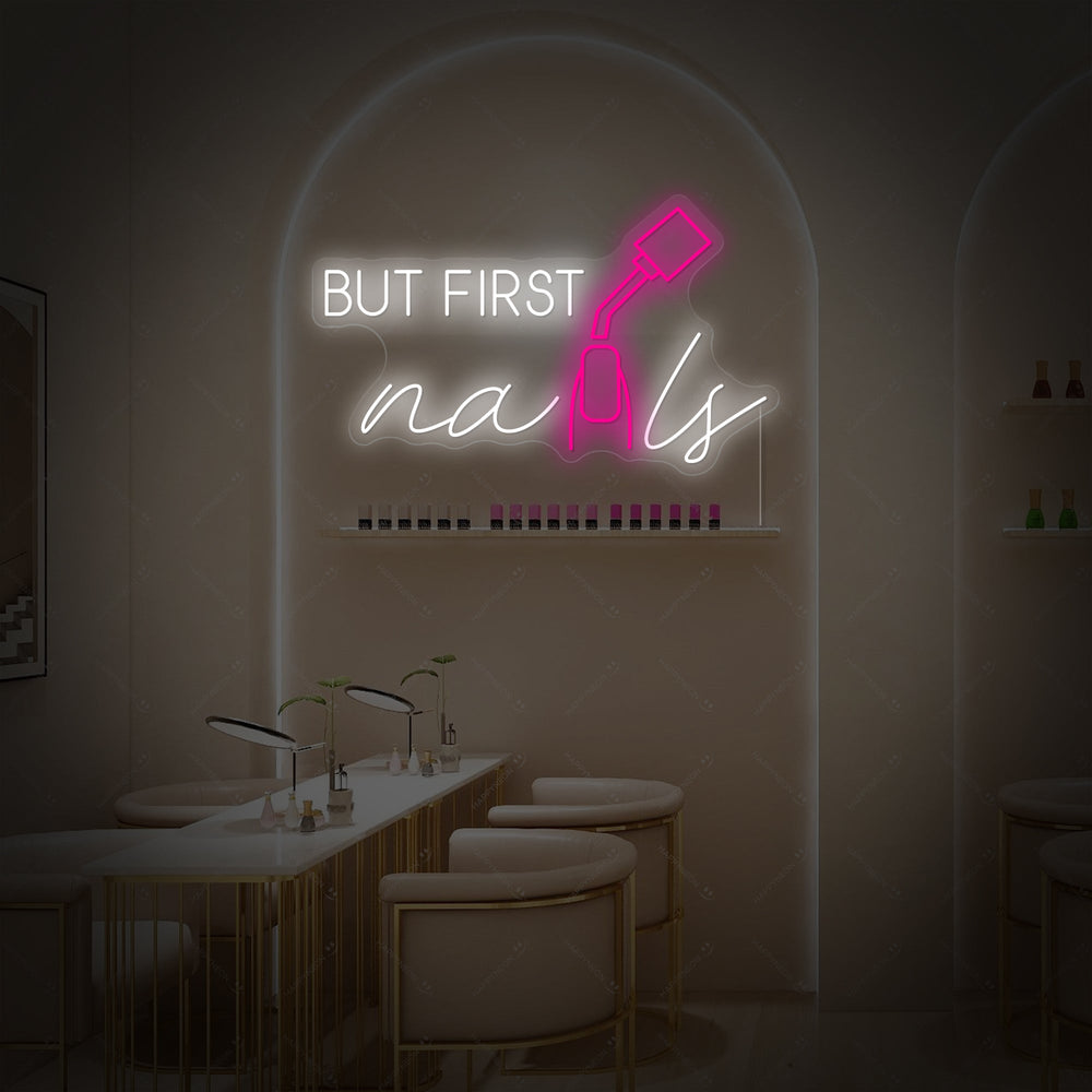 'But First Nails' pink neon script sign mounted on a textured wall.