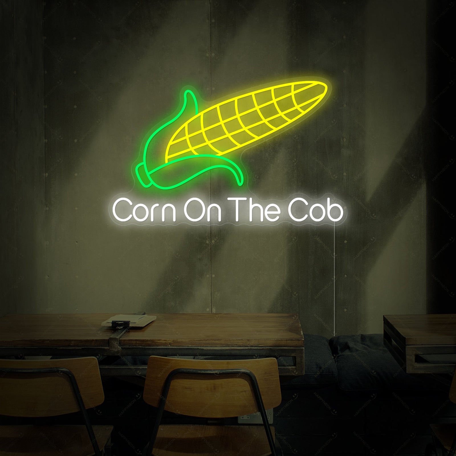 A glowing neon sign of a corn on the cob with the text 'Corn On The Cob' underneath it, shown with a clear acrylic backing against an interior brick wall.