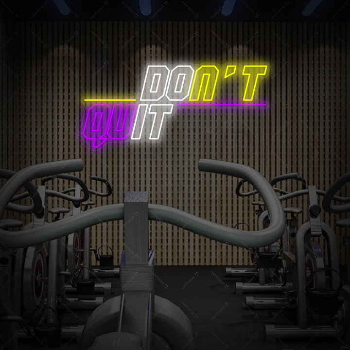 A glowing 'Don't Quit Do It' neon sign in red and blue, mounted on a brick wall above a workbench with dumbbells in a gym.