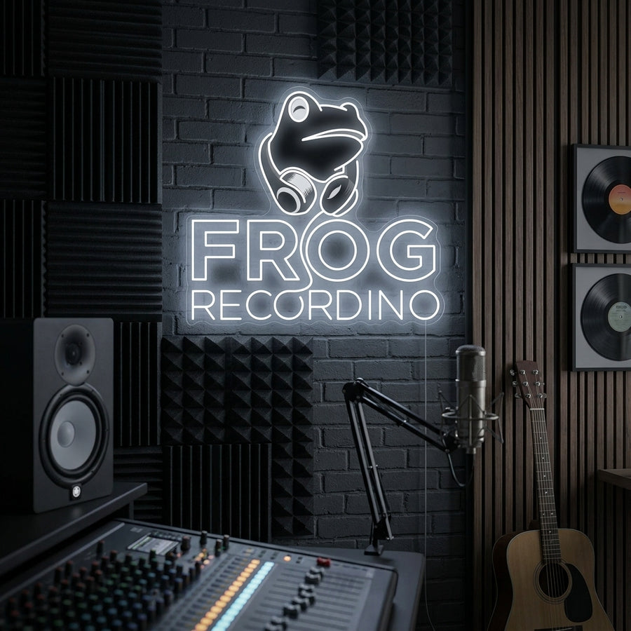 A illuminated neon sign showing a cartoon frog wearing headphones and using a mixing desk, with glowing text above reading 'FROG RECORDING', mounted on an exposed brick wall.