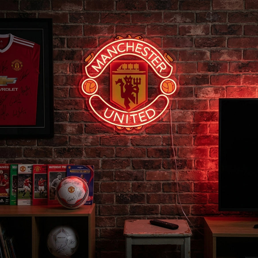 A lifestyle photo of a Manchester United football club neon sign glowing red on a wooden wall above a couch.