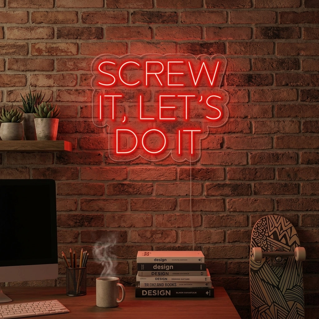 A person sitting at a desk in an office, working on a laptop, with a pink illuminated 'SCREW IT LETS DO IT' neon sign hanging on the brick wall in the background.