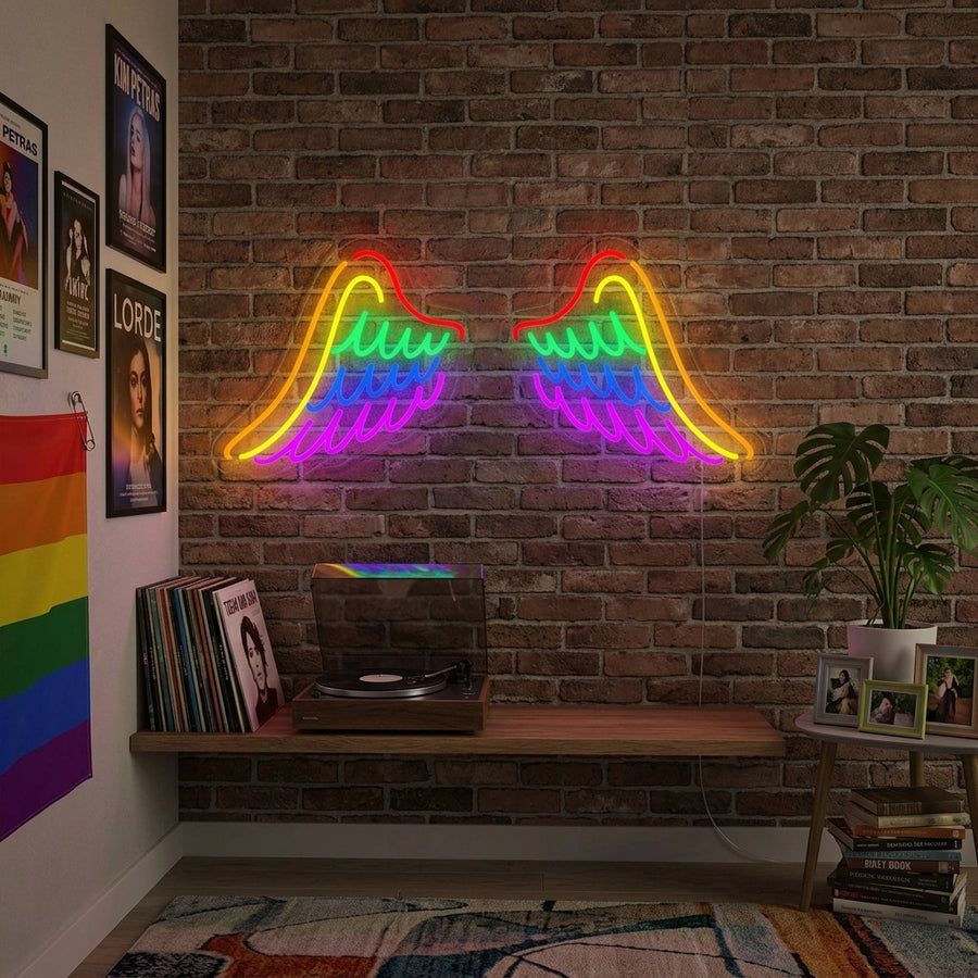 Illuminated rainbow wings neon sign mounted above a bed in a modern, stylish bedroom, creating a warm pride-themed atmosphere.