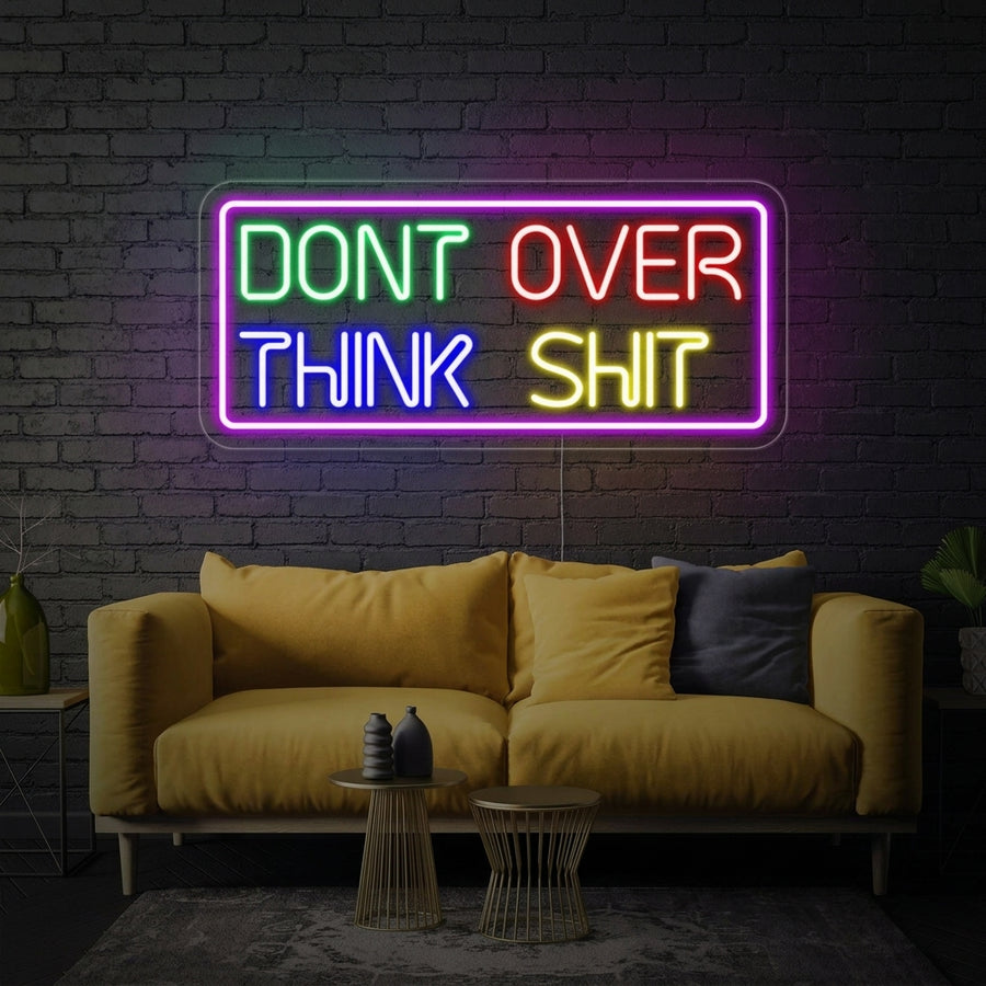 Handwritten-style 'Dont Over Think Shit' neon sign in bright pink script glowing on a textured brick wall in a cozy room.