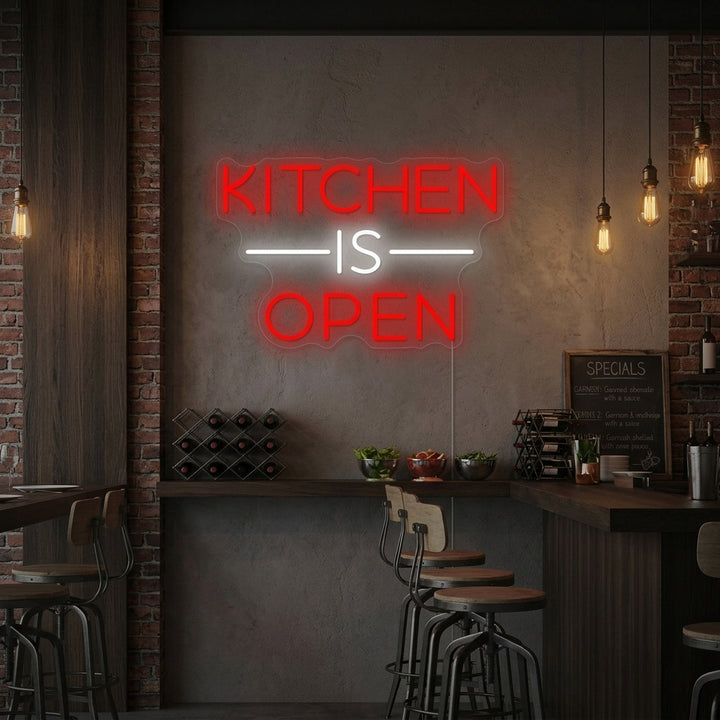 A "Kitchen Is Open" neon sign glowing warmly above a rustic wooden shelf with kitchen decor in a home setting.