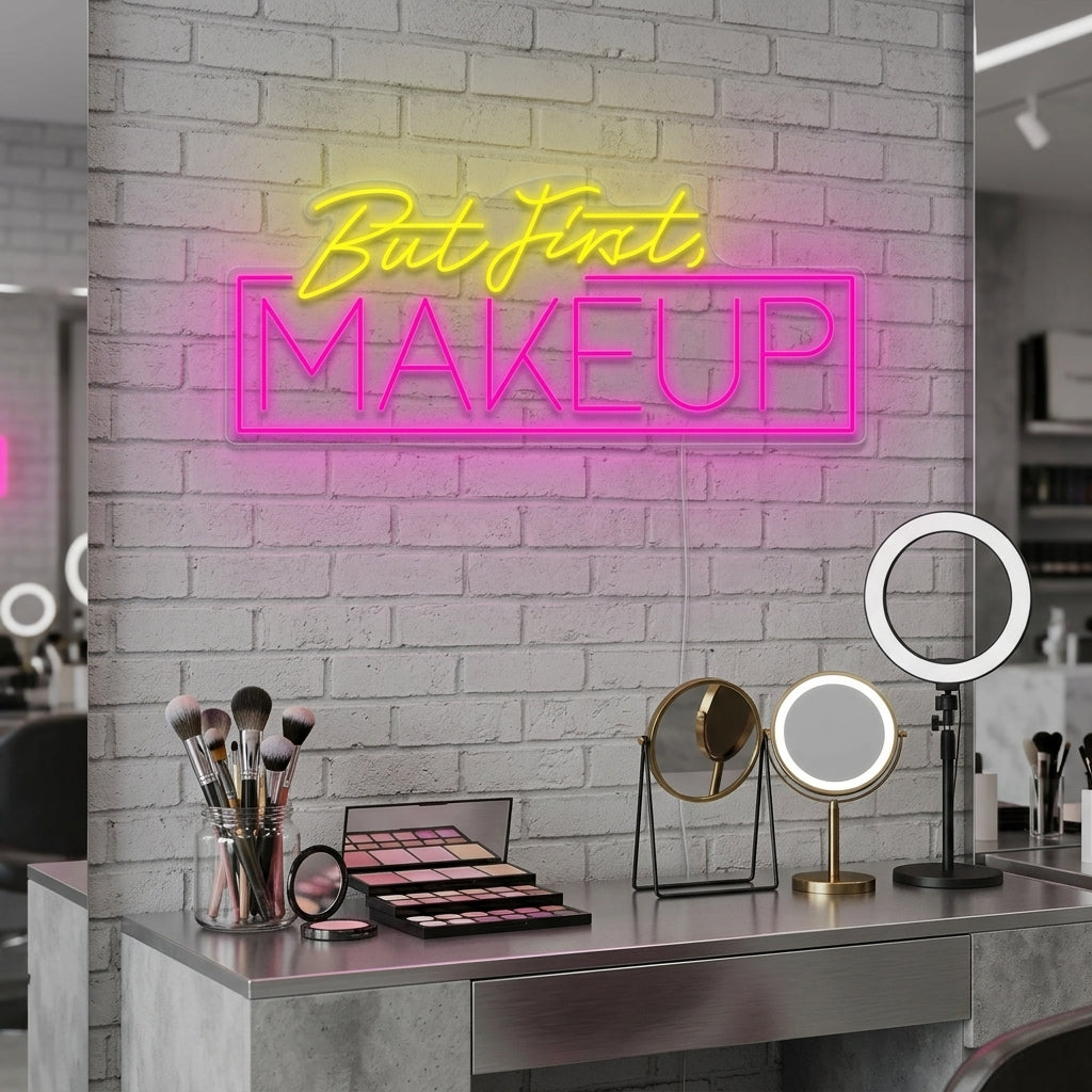 Handmade 'But First Makeup' script neon sign glowing in bright pink above a minimalist vanity setup with mirrors and makeup brushes.