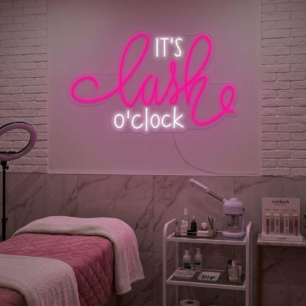 'Its Lashes Oclock' pink neon sign glowing brightly on a textured gray wall, creating a playful and glamorous atmosphere in a beauty studio setting.