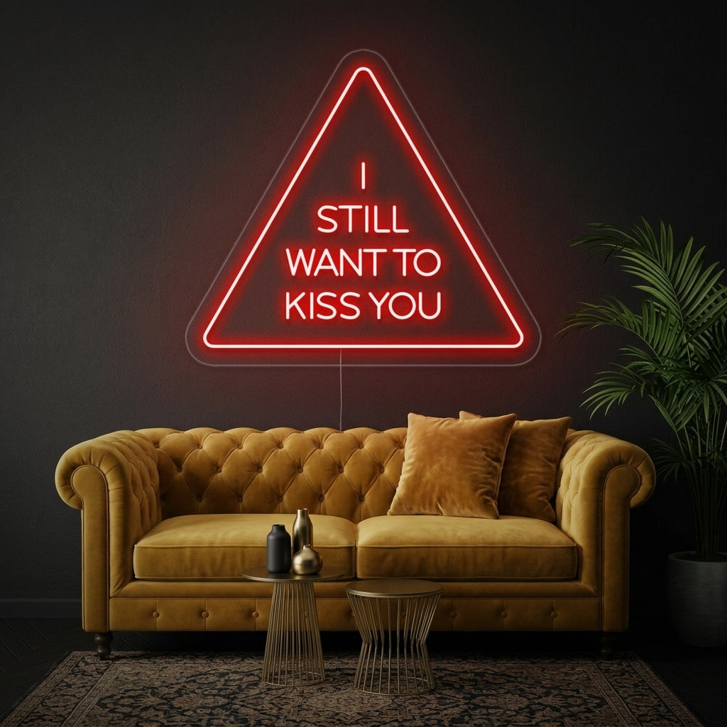 Handwritten style 'I Still Want To Kiss You' neon sign lit up in pink on a bedroom wall above a cozy bed.