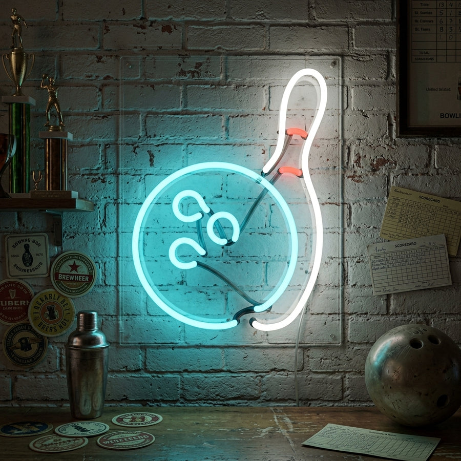 Bowling-themed neon table sign displaying glowing red bowling pins and a ball on a desk in a home game room setting.