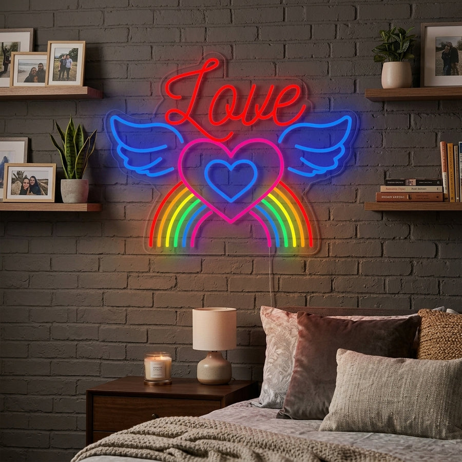 A lifestyle photo showing the 'LGBT Love Rainbow Wings' neon sign mounted above a bed in a warm bedroom setting.
