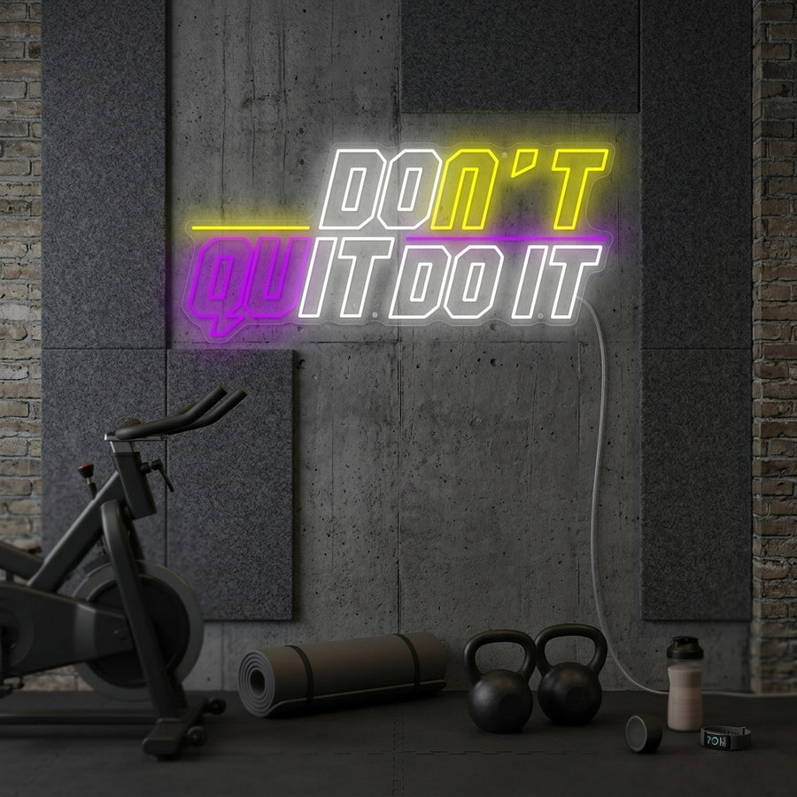 A 'Don't Quit Do It' neon sign with changing colors, glowing as motivational wall decor in a home gym or workout space.