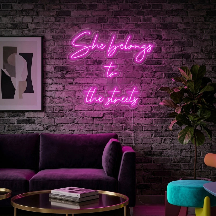 White glowing text 'She Belongs To The Streets' neon sign on a charcoal grey brick wall in a modern living room