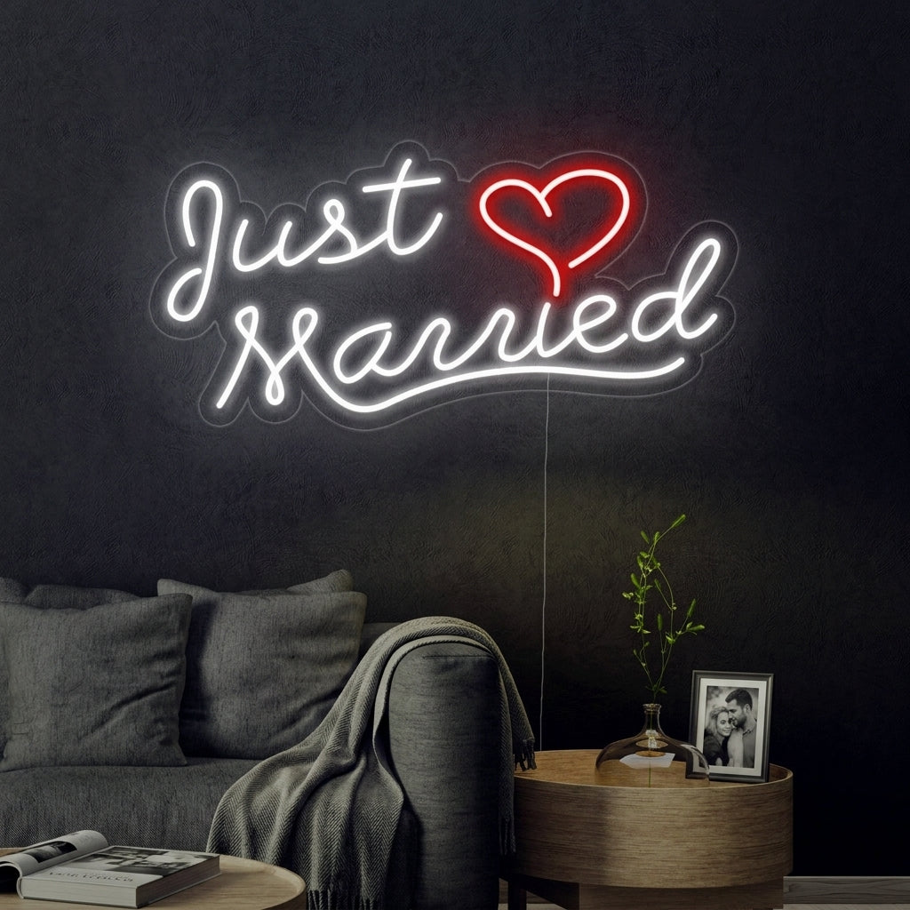 A candid style photo of a modern outdoor wedding reception where a glowing white 'Just Married' neon sign is mounted on a decorated archway over the newlyweds' sweetheart table at dusk.