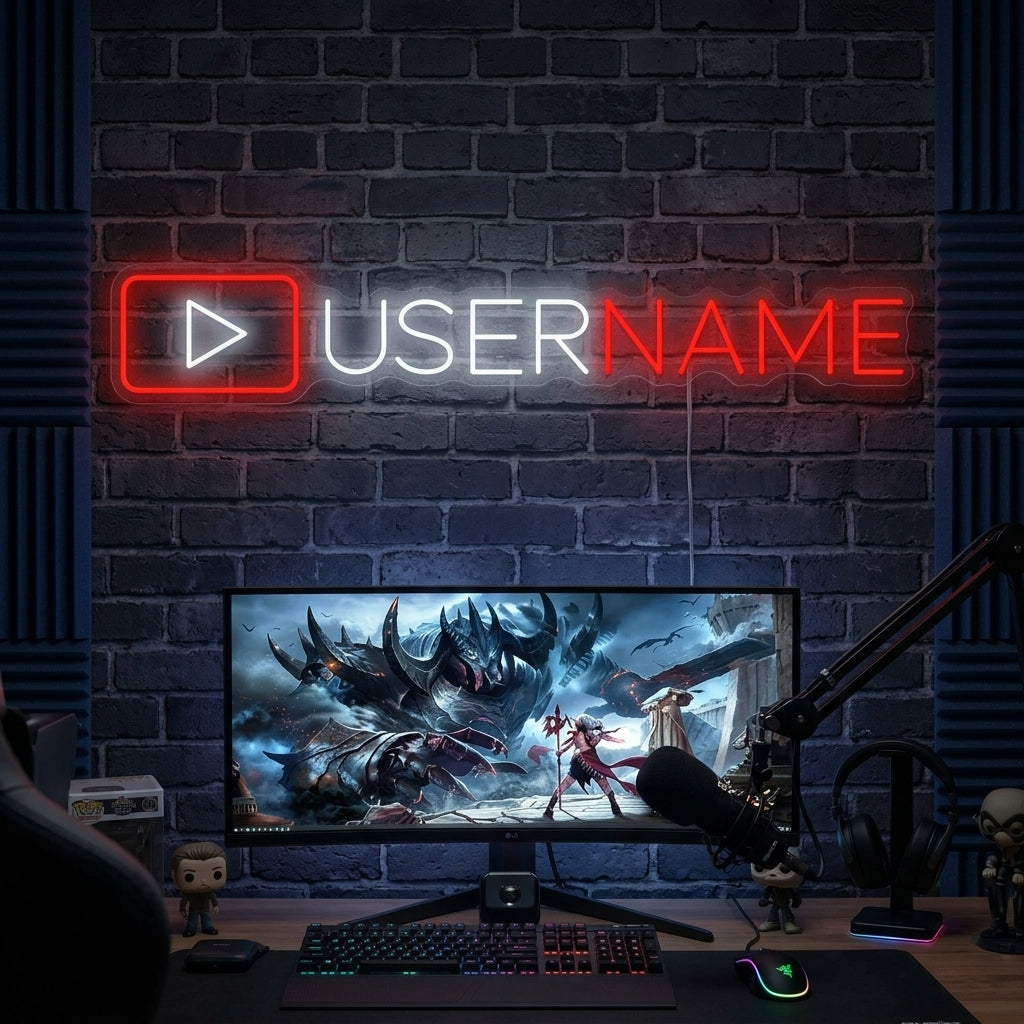 A custom YouTube logo neon sign with personalized text and a camera icon, glowing on a dark wall above a desk setup with a computer and plants.