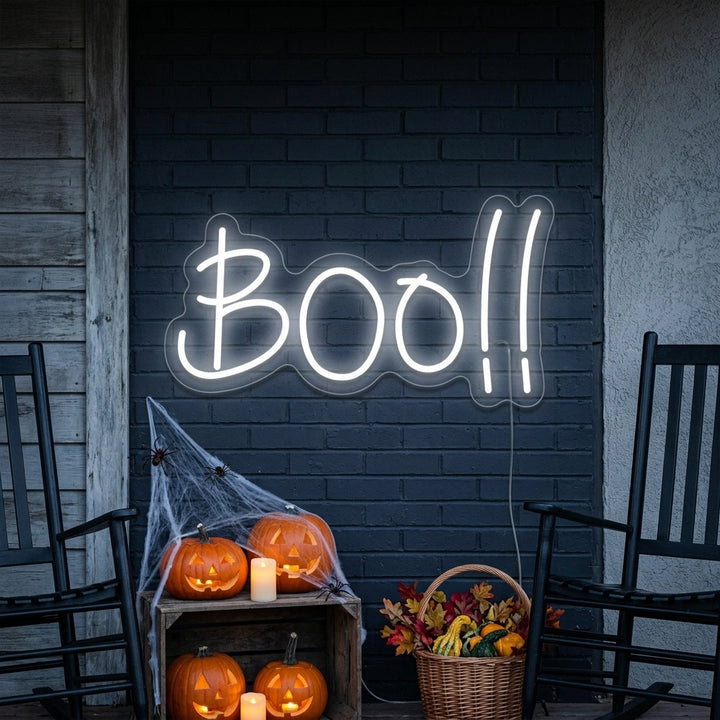 Illuminated Boo neon sign glowing on a textured brick wall with holiday decorations.