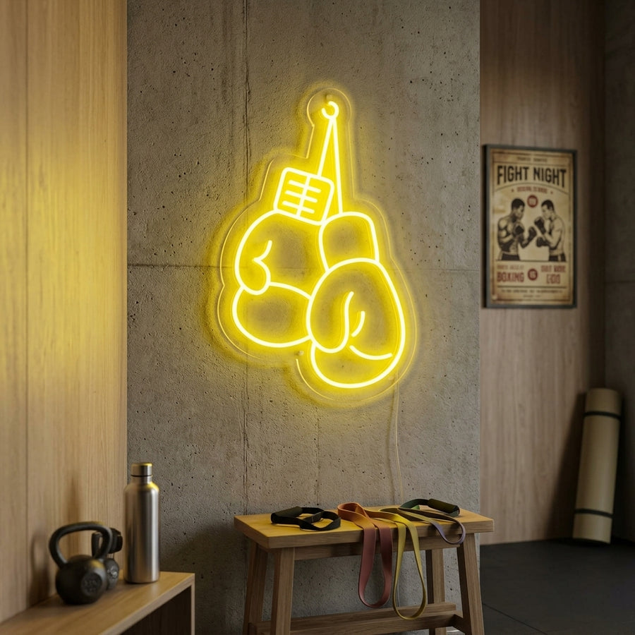 Illuminated neon sign depicting two crossed boxing gloves hanging on a textured dark gym wall above a punching bag.