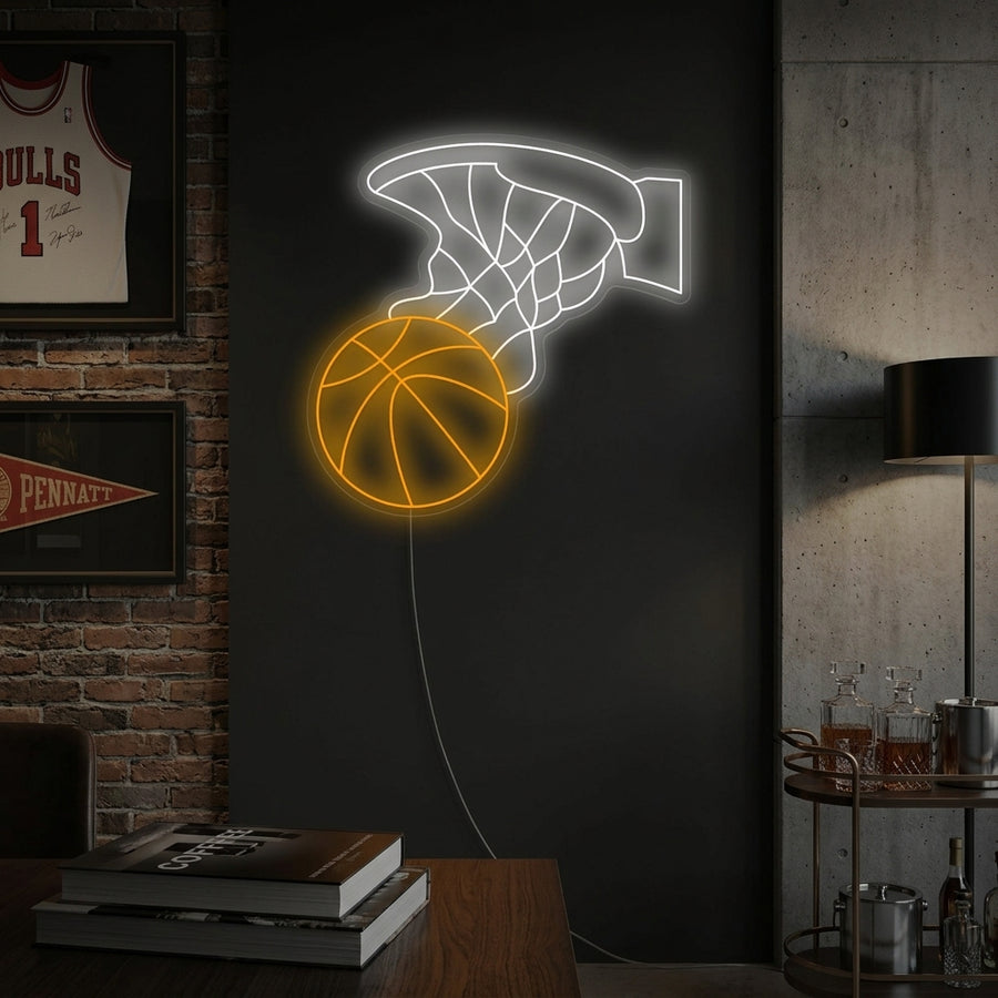 A glowing blue and orange basketball hoop neon sign mounted on a brick wall in a sports-themed room, showing a basketball going through the net.